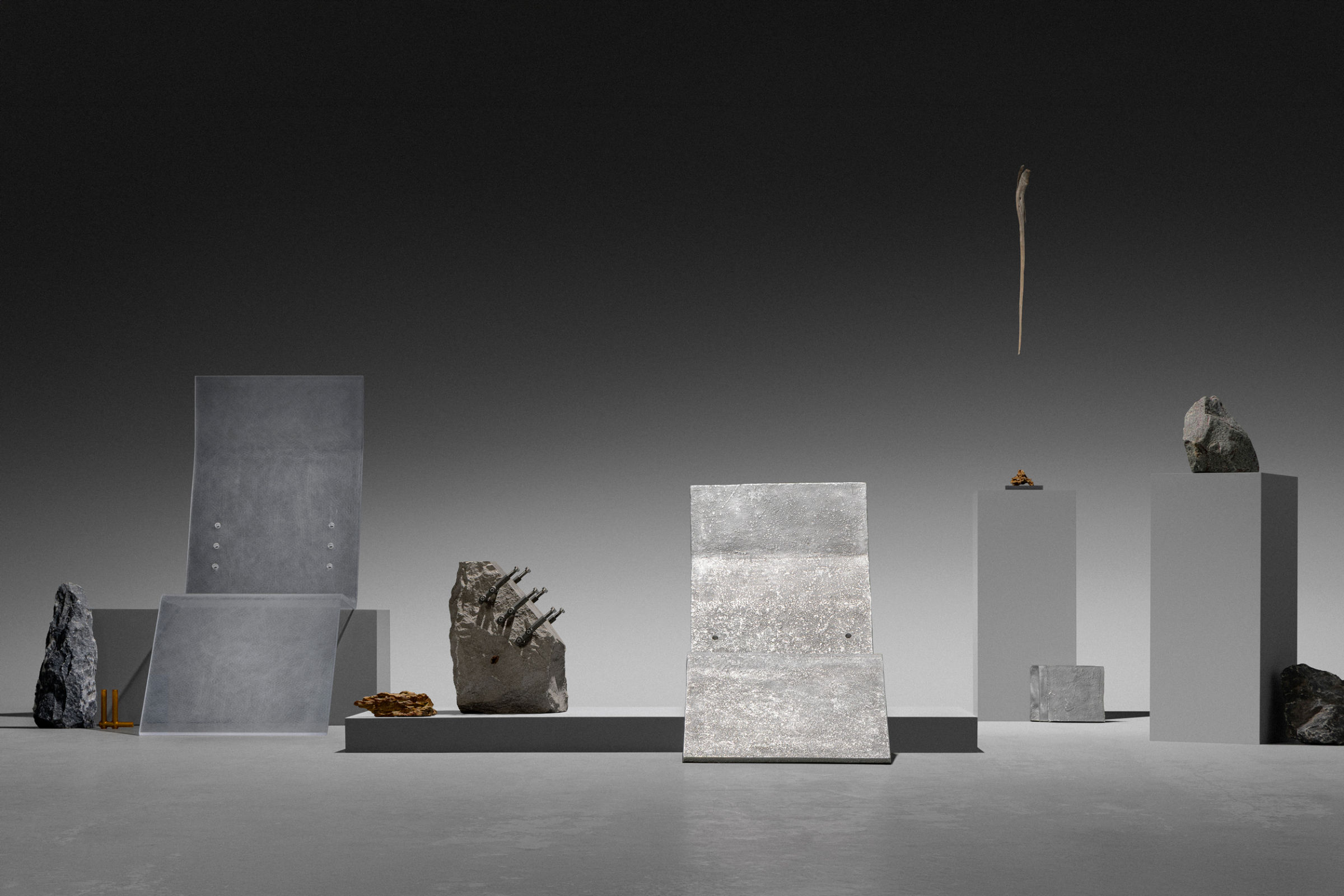 Wide view of the full studio set displaying an arrangement of metal, stone and cast sculptures on white pedestals across a gradient grey background.